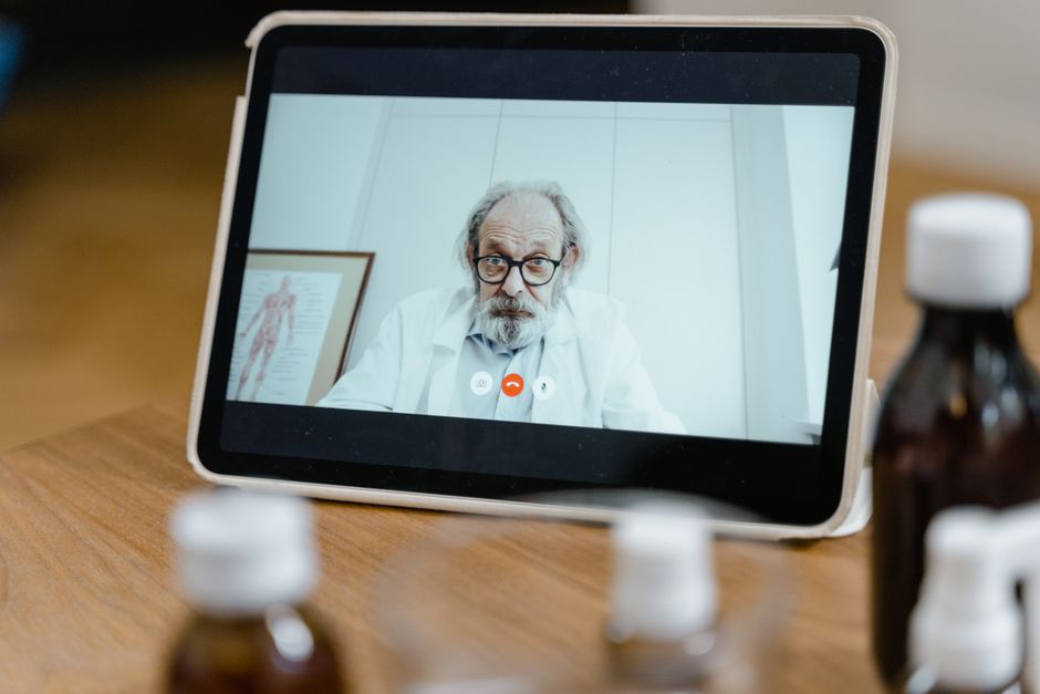 Acessibilidade Brasil — Elderly male doctor in white coat on a digital tablet screen during a virtual medical consultation.