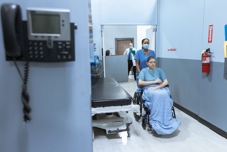 Acessibilidade Brasil — A nurse helps a patient in a wheelchair down a hospital corridor, reflecting care and medical