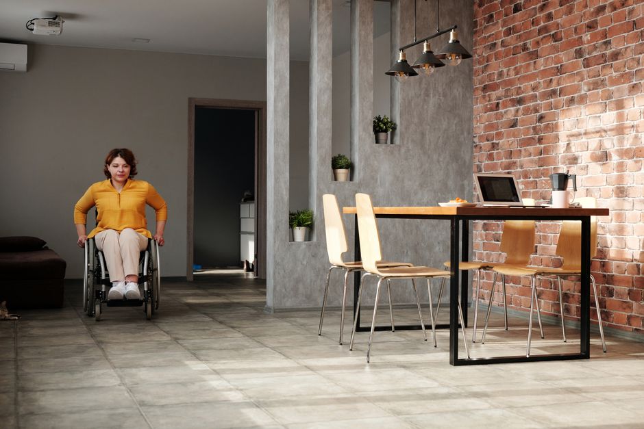 Acessibilidade Brasil — A woman in a wheelchair navigating a modern home office space with brick walls.