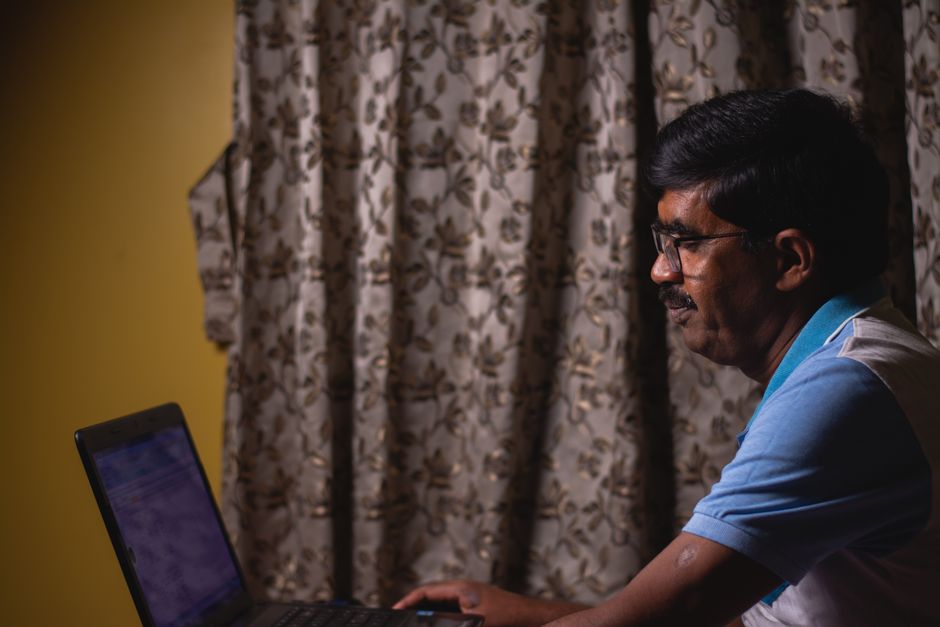 Acessibilidade Brasil — A man with glasses using a laptop at home, focusing on work.