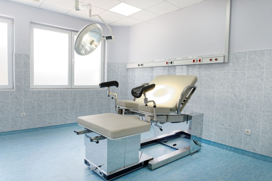 Acessibilidade Brasil — Bright gynecological examination room with adjustable chair and overhead light in a medical facility.