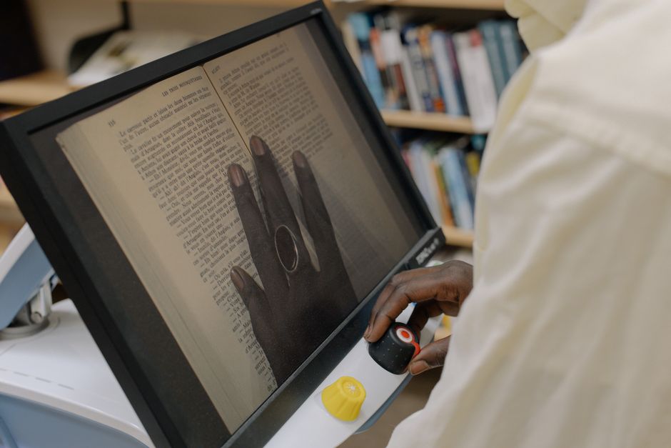 Acessibilidade Brasil — Person using a digital magnifier to read a book, enhancing text accessibility.