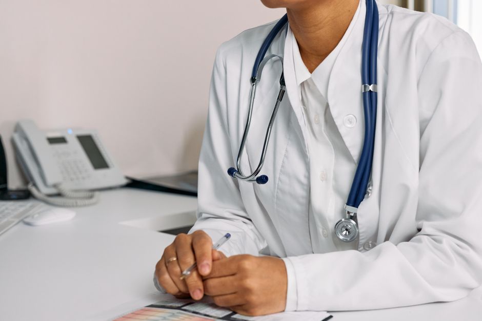 Acessibilidade Brasil — Doctor with stethoscope and white coat seated at a clinic desk.