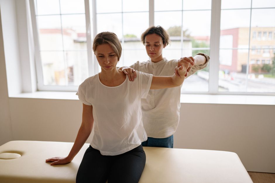 Acessibilidade Brasil — A therapist assists a woman with arm stretching during a physical therapy session in a bright