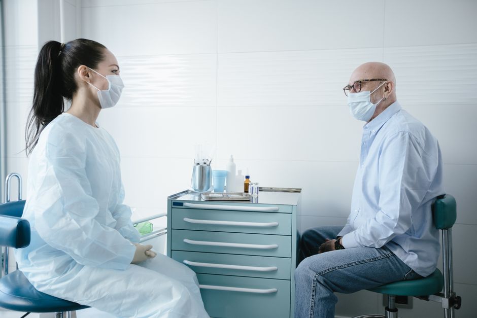Acessibilidade Brasil — Medical professional consults a senior patient, both wearing masks in a clinic setting.