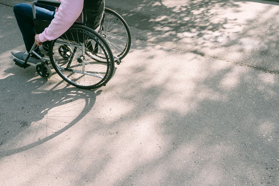 Acessibilidade Brasil — A person in a wheelchair navigating a sunlit road with tree shadows. The image captures a moment of