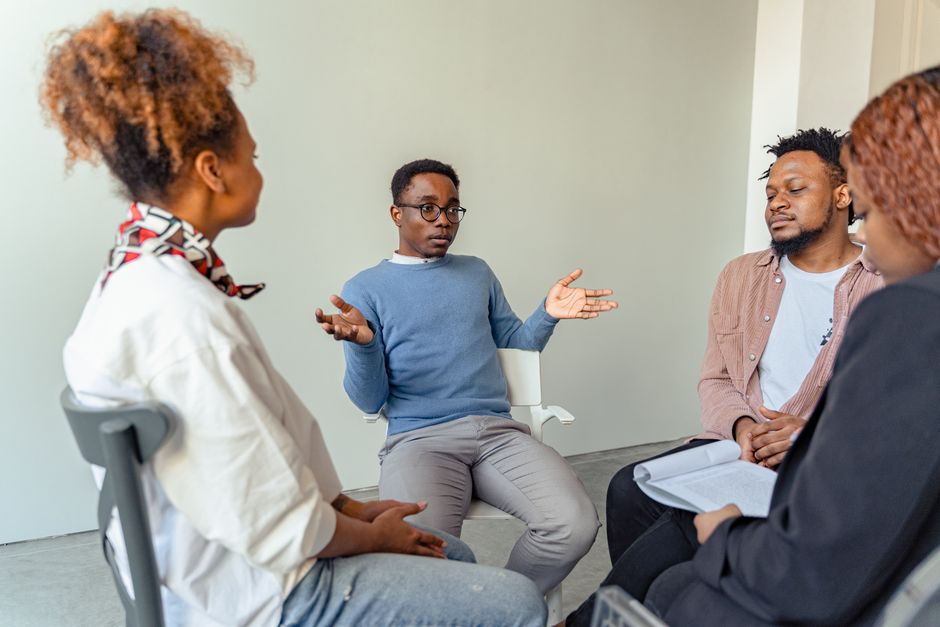Acessibilidade Brasil — Diverse group therapy session with young adults and a mental health professional indoors.