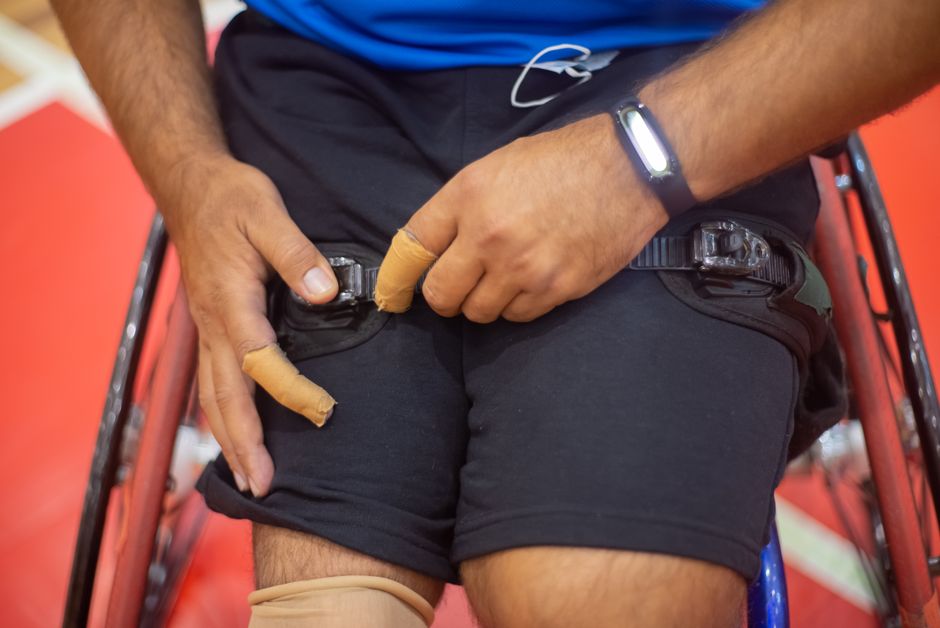 Acessibilidade Brasil — Close-up image of an athlete adjusting straps on a wheelchair indoors.