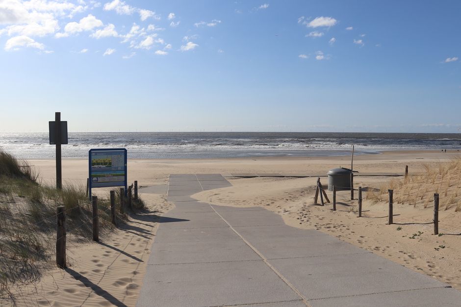 Acessibilidade Brasil — Tranquil beachside walkway framed by sand dunes leading to the ocean under a clear blue sky.